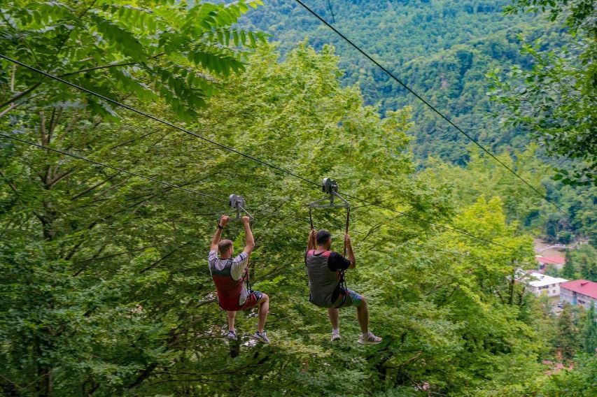 Zwei Personen an einer Zipline über bewaldetem Tal